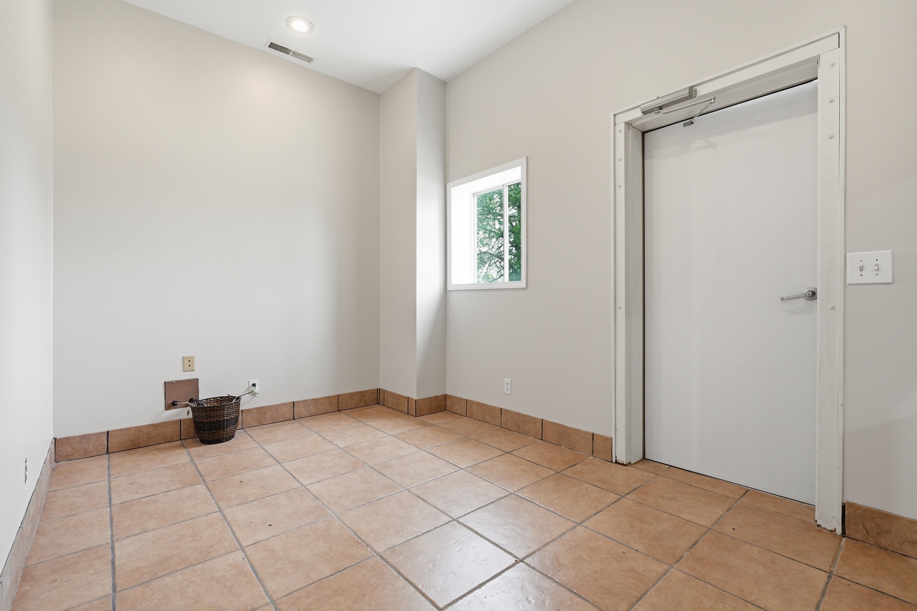 Small utility room with tile floor, single window letting in soft daylight, simple wainscot trim, electrical outlets ready for appliances, and an interior door leading to the rest of the house