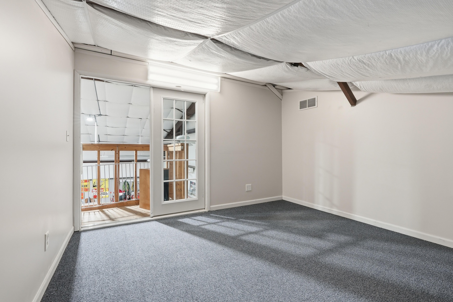 Unfinished basement bonus room with carpet flooring, French doors opening to the lower-level family area, exposed insulation on the ceiling, walls already drywalled and painted, ready for finishing