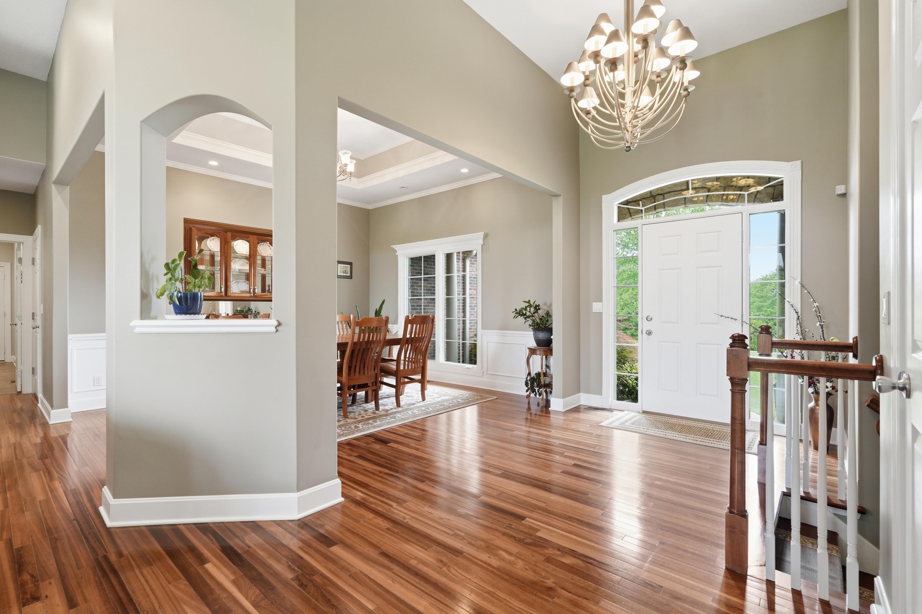 Entry foyer with an iron-and-glass chandelier hanging from the high ceiling, exotic hardwood floors stretching in every direction, an arched front door with transom and sidelights, and openings into the dining room and great room on either side
