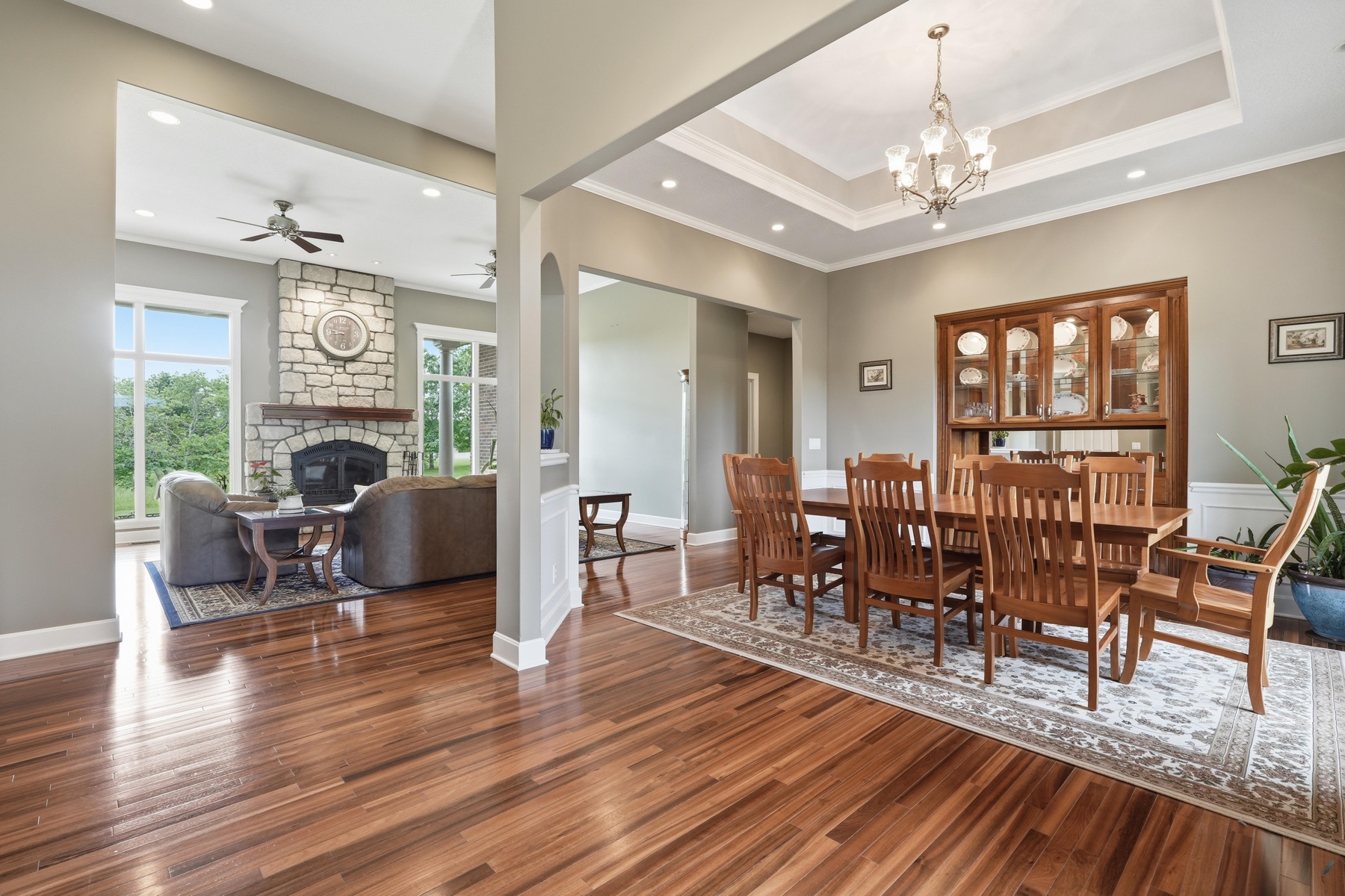 Open view through the home showing the formal dining room with tray ceiling on the right and the great room with stone fireplace on the left, separated by a single column, hardwood stretching the length of both rooms
